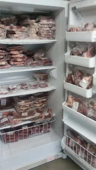 Upright freezer, doors opened, shelves filled with frozen beef cuts.