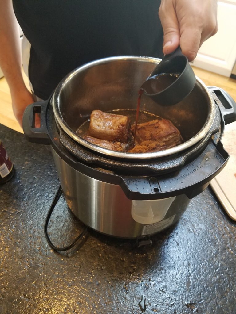 Pouring Worcestershire and Soy sauce over cooking ribs.
