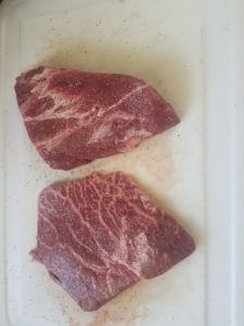 Two raw seasoned flat iron steaks.